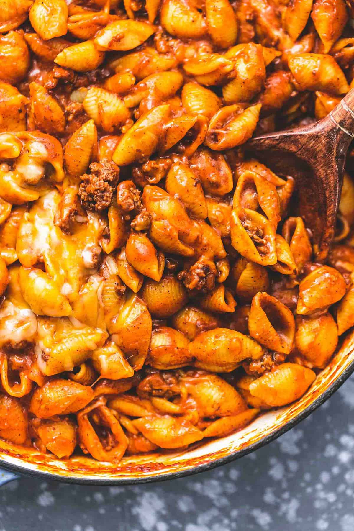 close up top view of beefy enchilada shells with a wooden serving spoon in a pan.