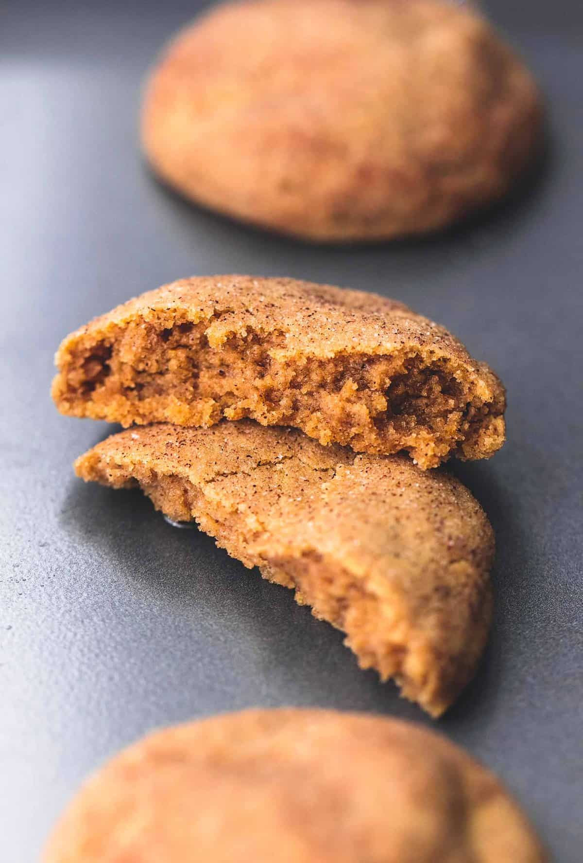 close up of a pumpkin snickerdoodle broken in half with one half on top of the other with more cookies on the side.