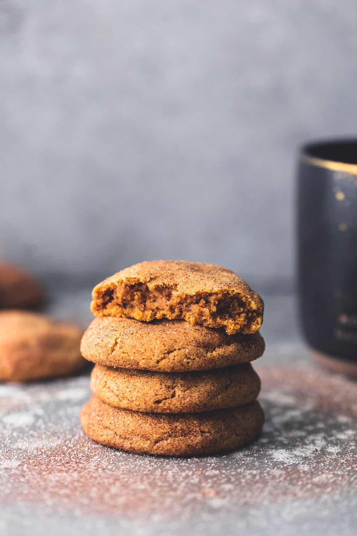 stacked pumpkin snickerdoodles with the top cookie missing a bite with more cookies and a mug barely visible on the sides.