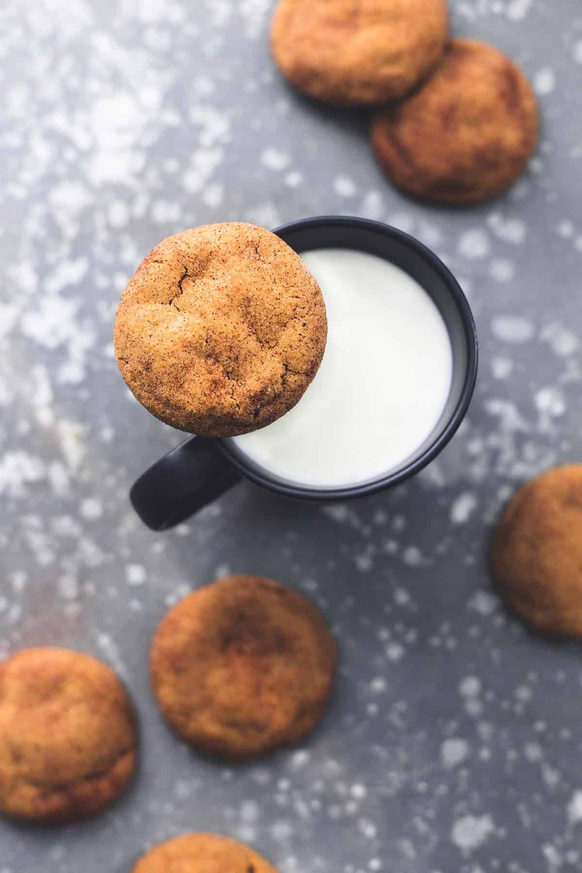 top view of a pumpkin snickerdoodle sitting on top of a mug of milk with more cookies on the side.