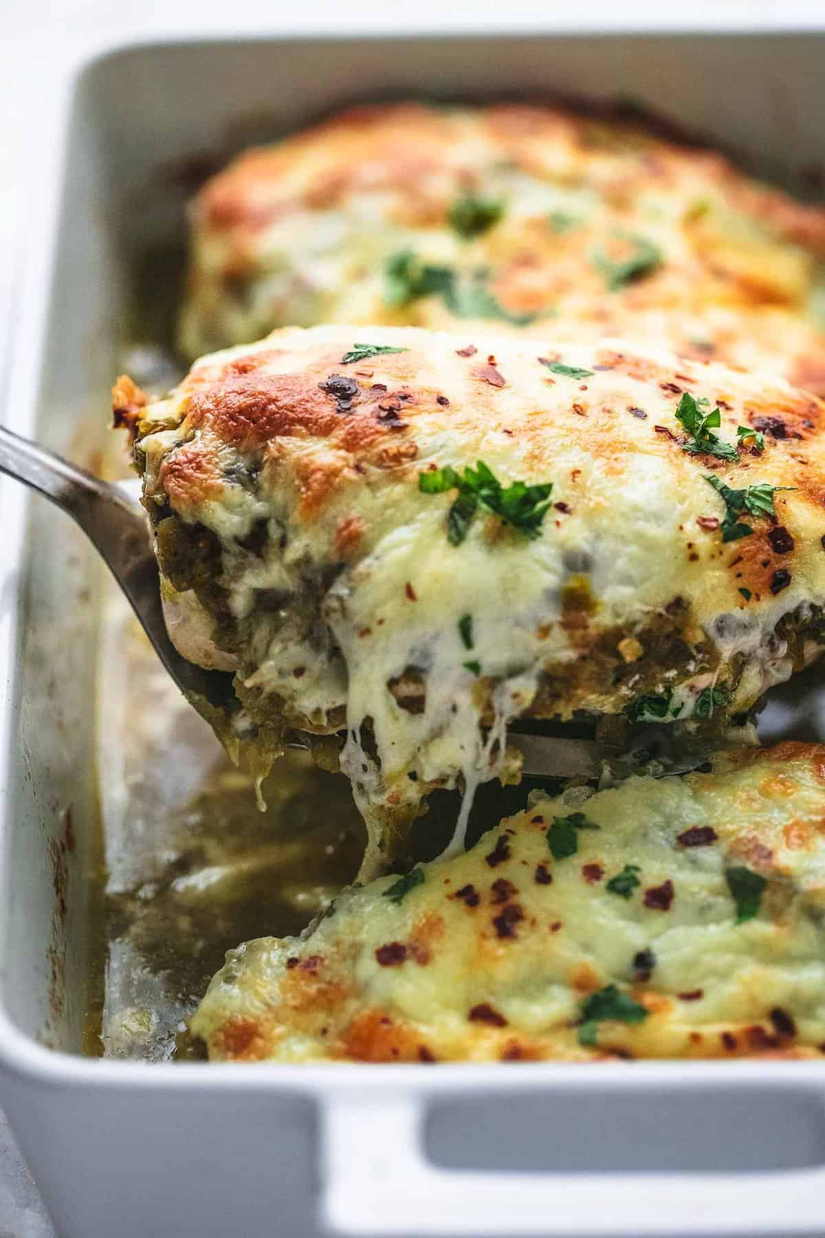 a piece of baked salsa verde chicken being lifted by a spatula from a baking pan of more chicken. 