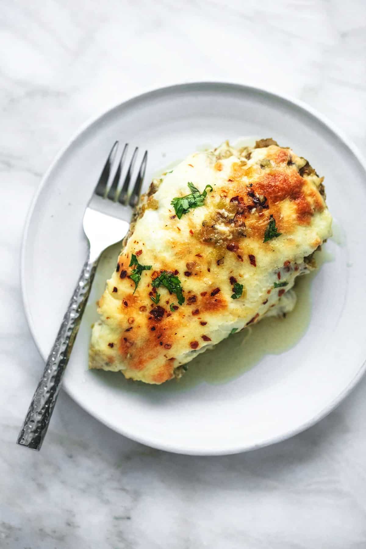 top view of a piece of baked salsa verde chicken with a fork on a plate.