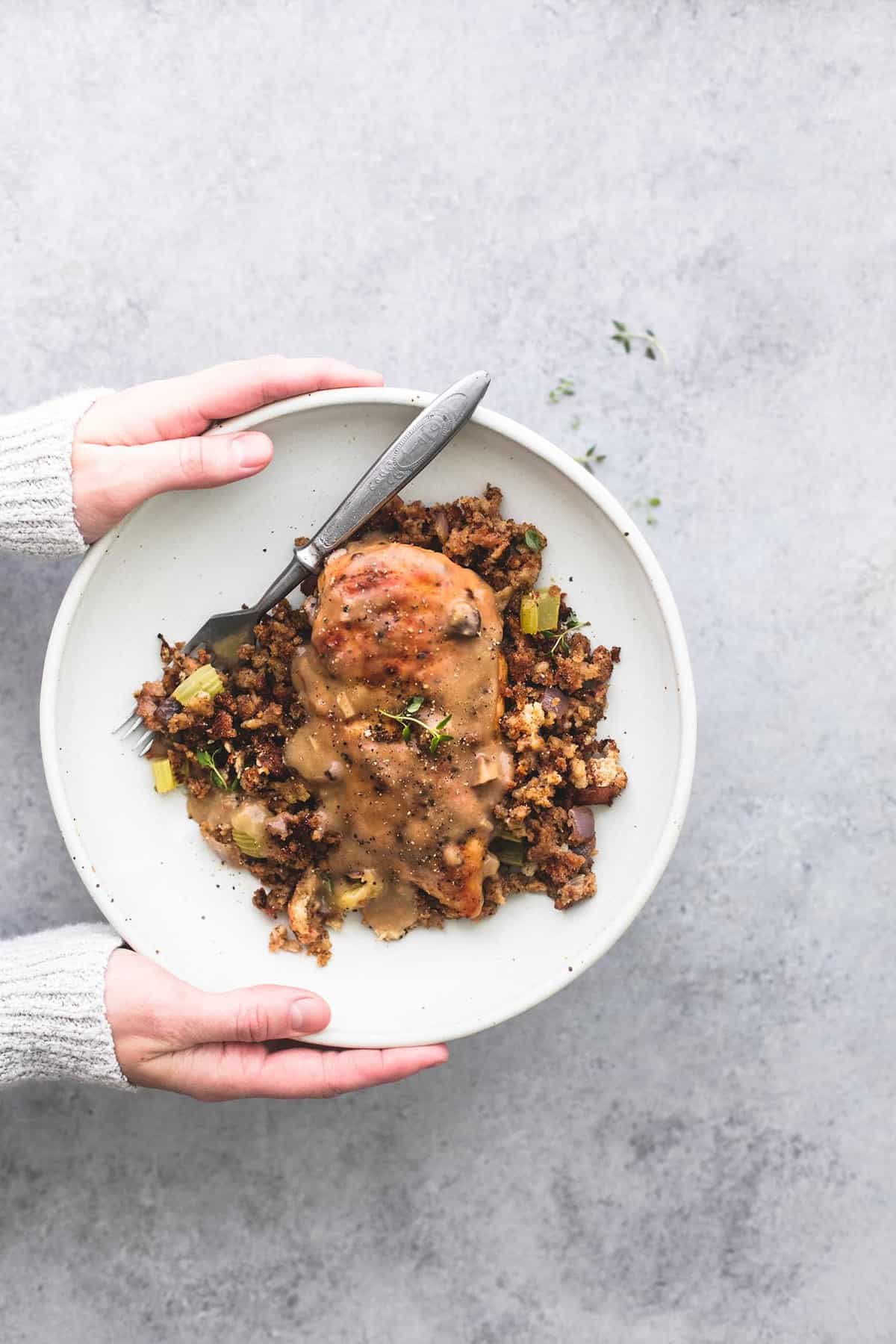 top view of a pair of hands holding a plate with a fork and skillet chicken and stuffing on it.