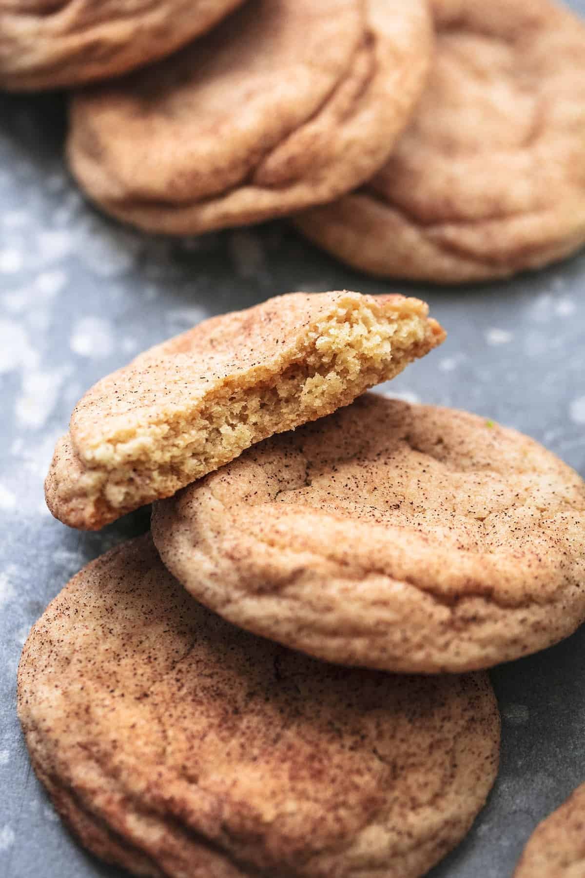 snickerdoodles overlapping one another with the top cookie missing a bite and more cookie in the background.