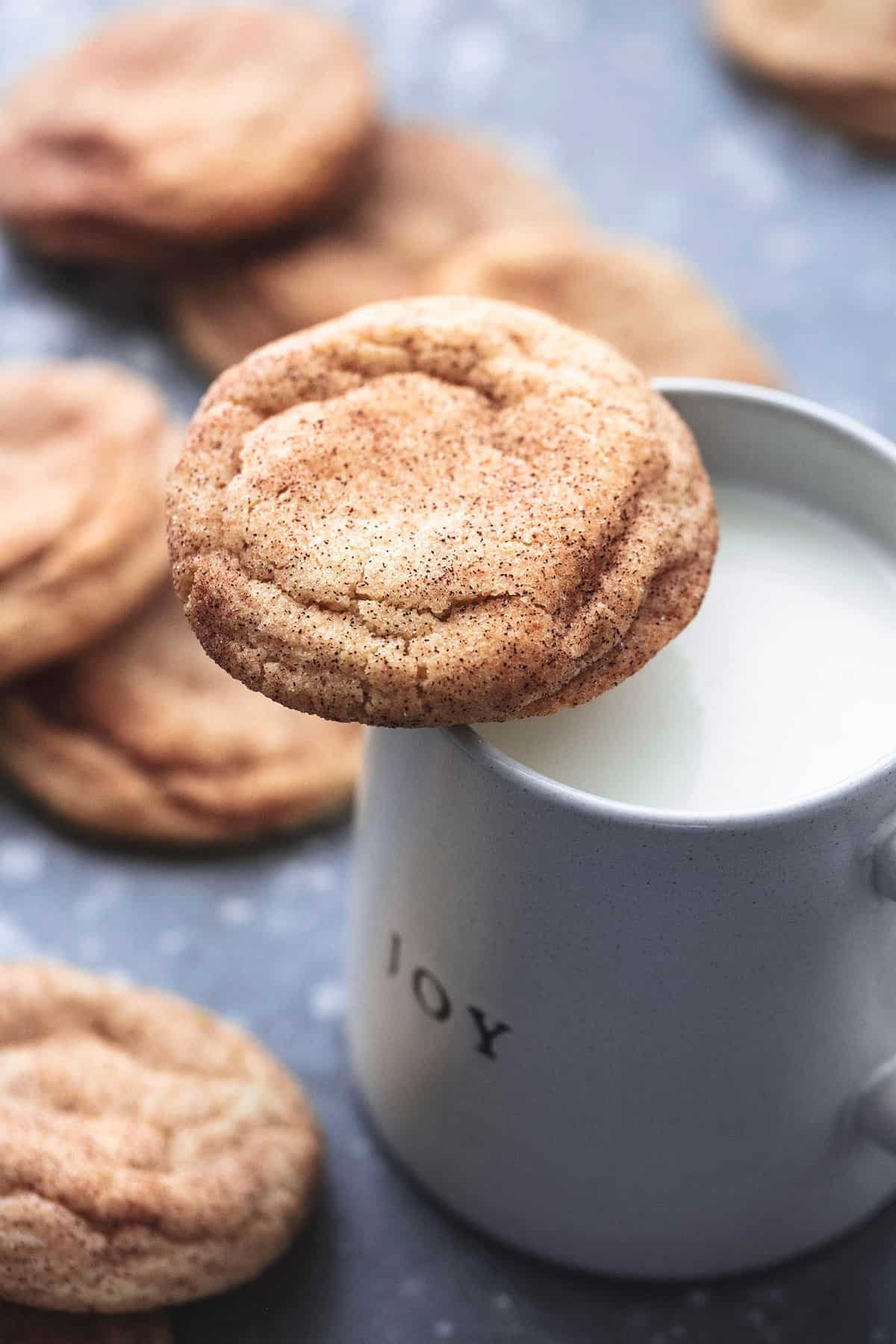 a snickerdoodle resting on top of a mug of milk with more cookies around it.