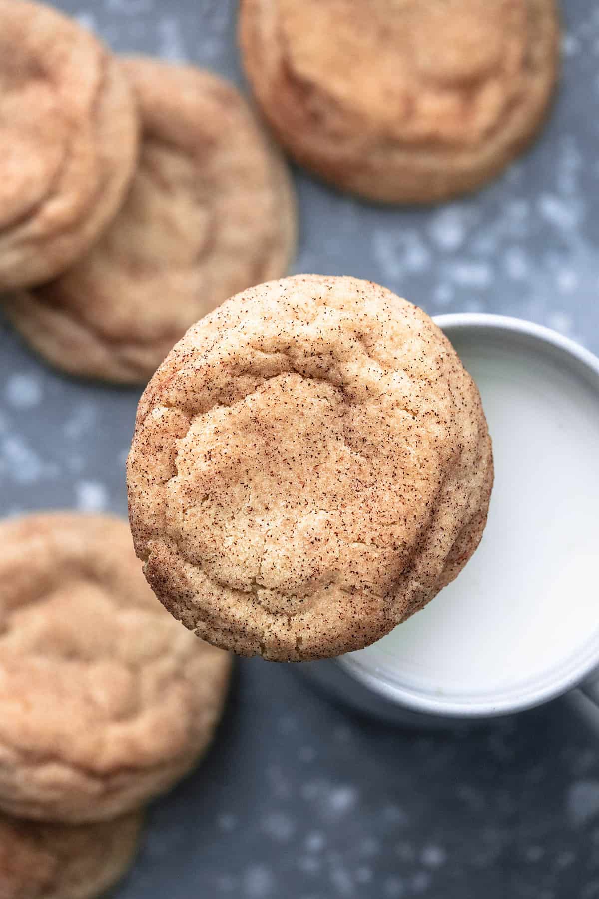 close up top view of a snickerdoodle resting on top of a mug of milk with more cookies around it.
