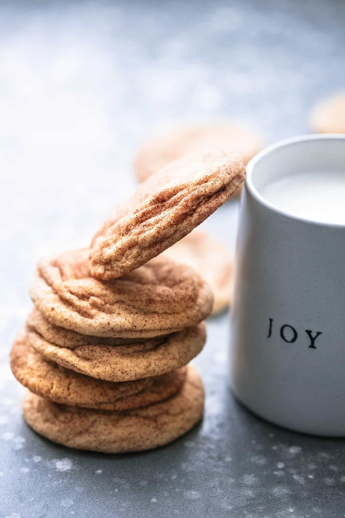 stacked snickerdoodles with the top cookie slanted to rest on a mug of milk.