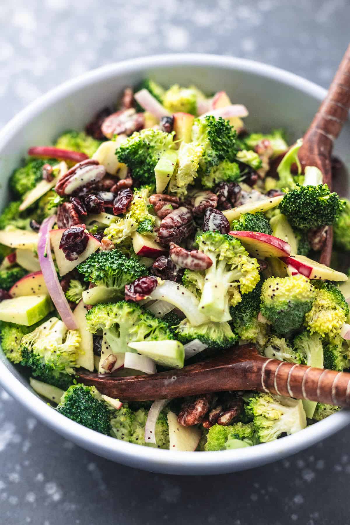 broccoli apple salad with poppyseed dressing with two wooden serving spoons in a bowl.