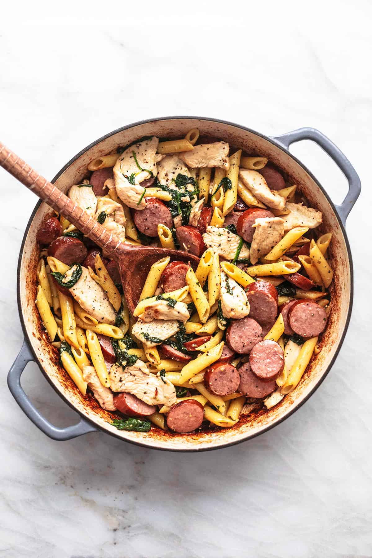 top view of chicken and sausage pasta with a wooden serving spoon in a pan.