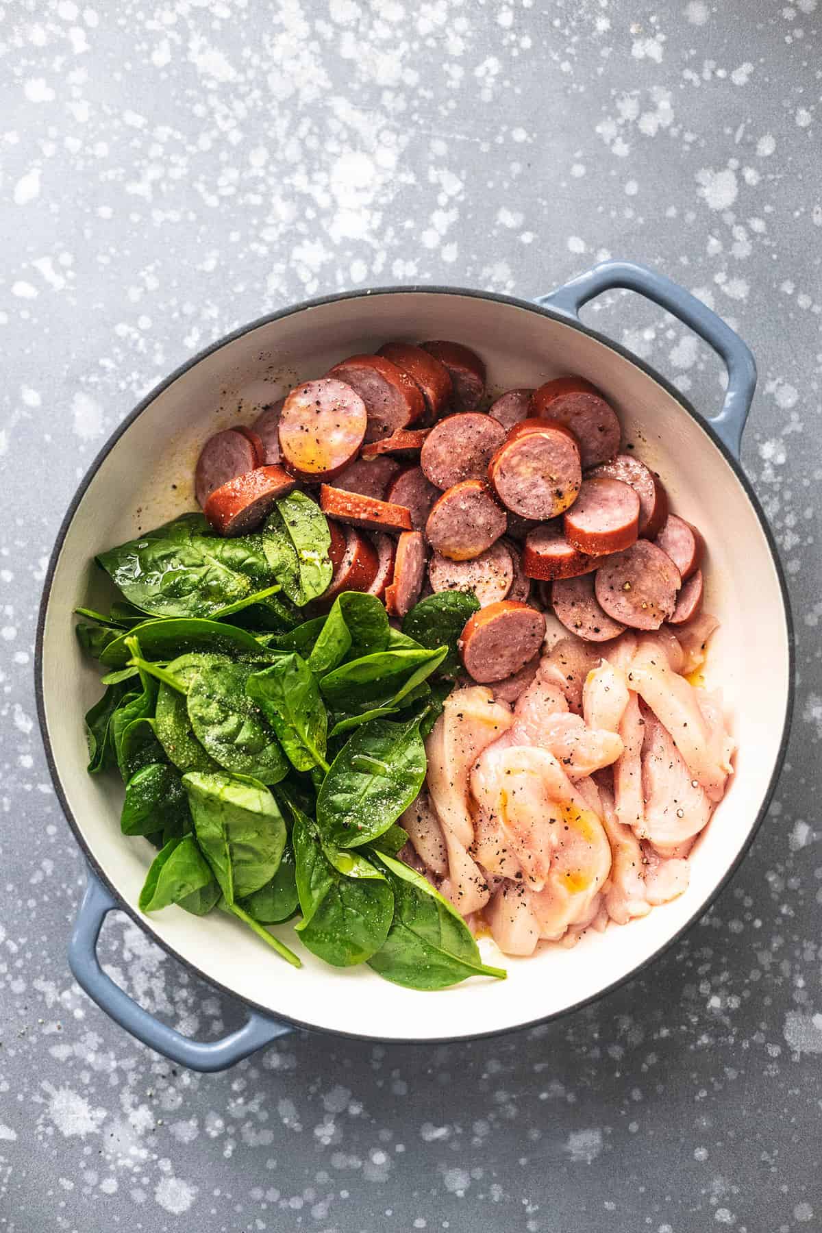 top view of uncooked chicken, sausage and spinach leaves in a pan.