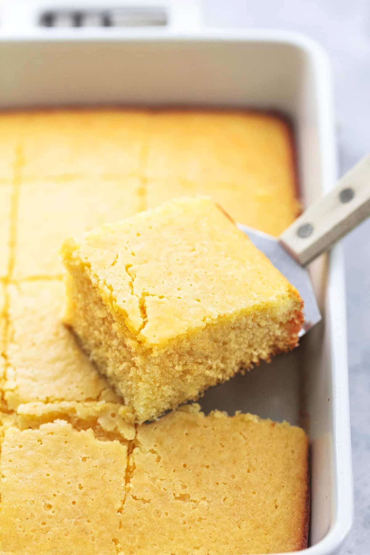 close up of a spatula with a piece of cornbread on it sitting on top of the rest of the cornbread in a baking pan.