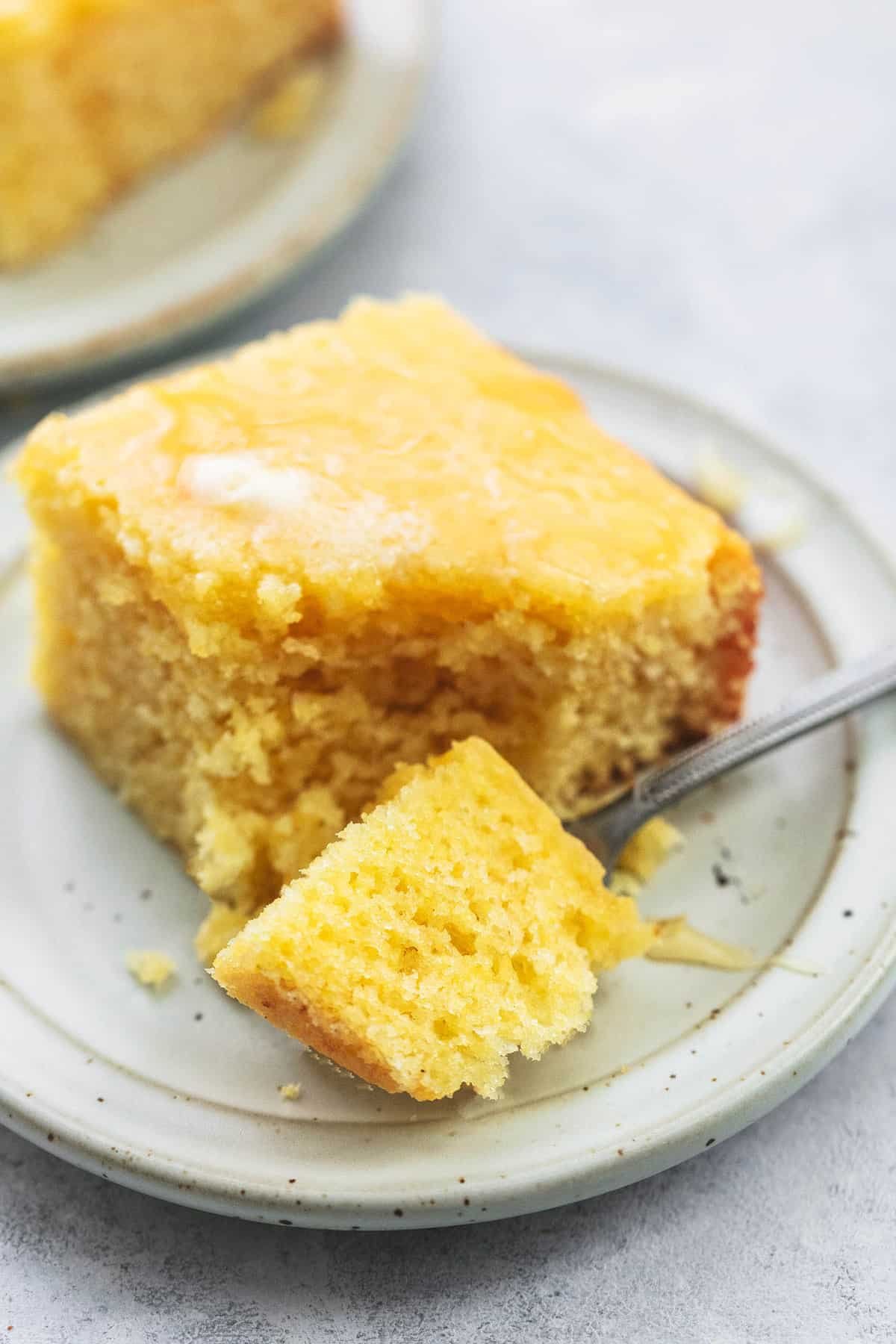 a bite of cornbread on a fork in front of the rest of the cornbread piece on a plate.