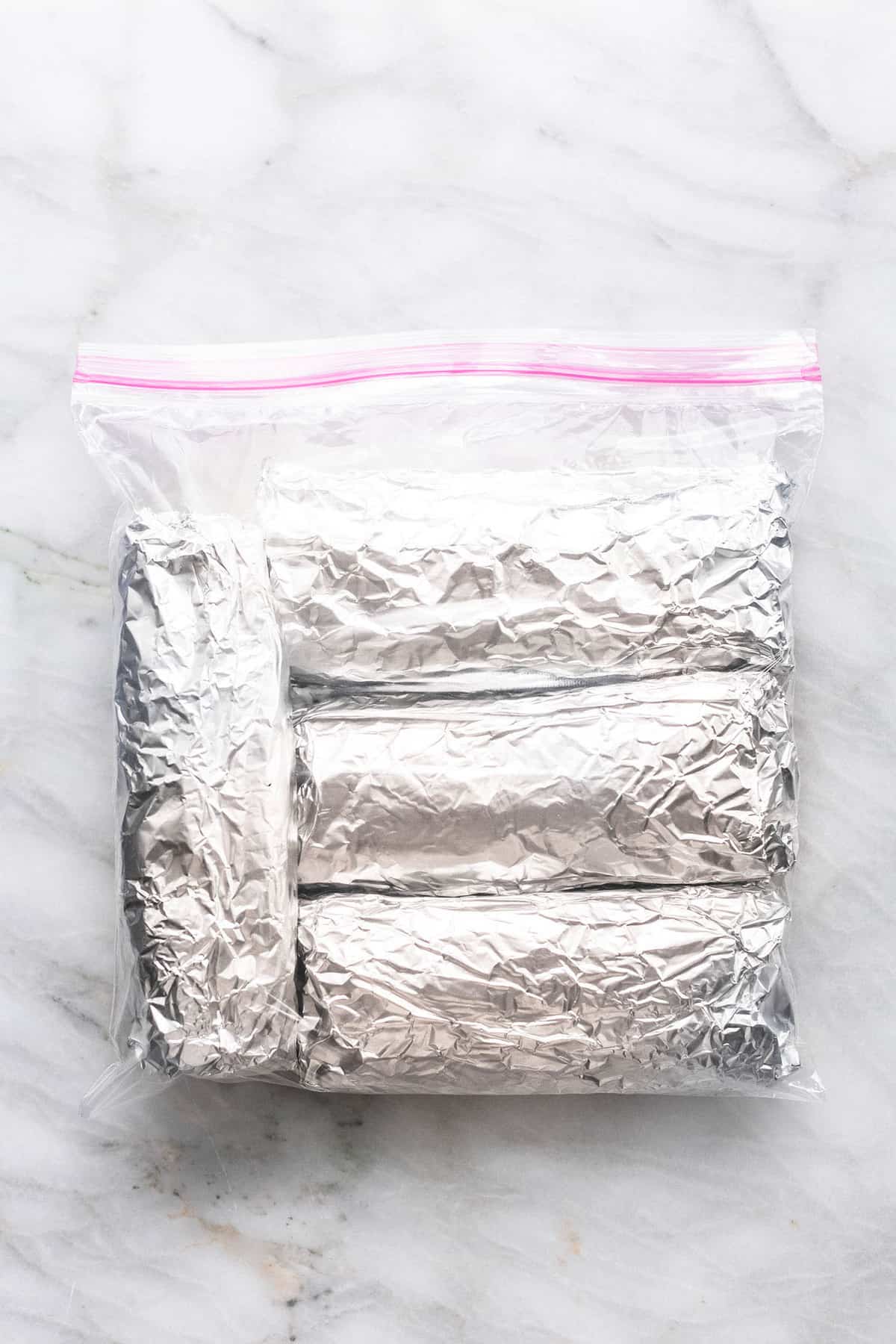 top view of freezer breakfast burritos wrapped in foil in a zip lock bag.