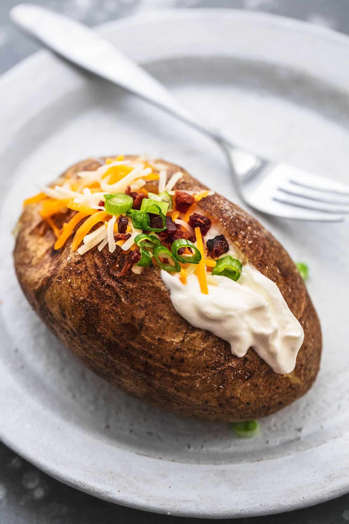 close up of an instant pot baked potato with topping and a fork on the side both on a plate.