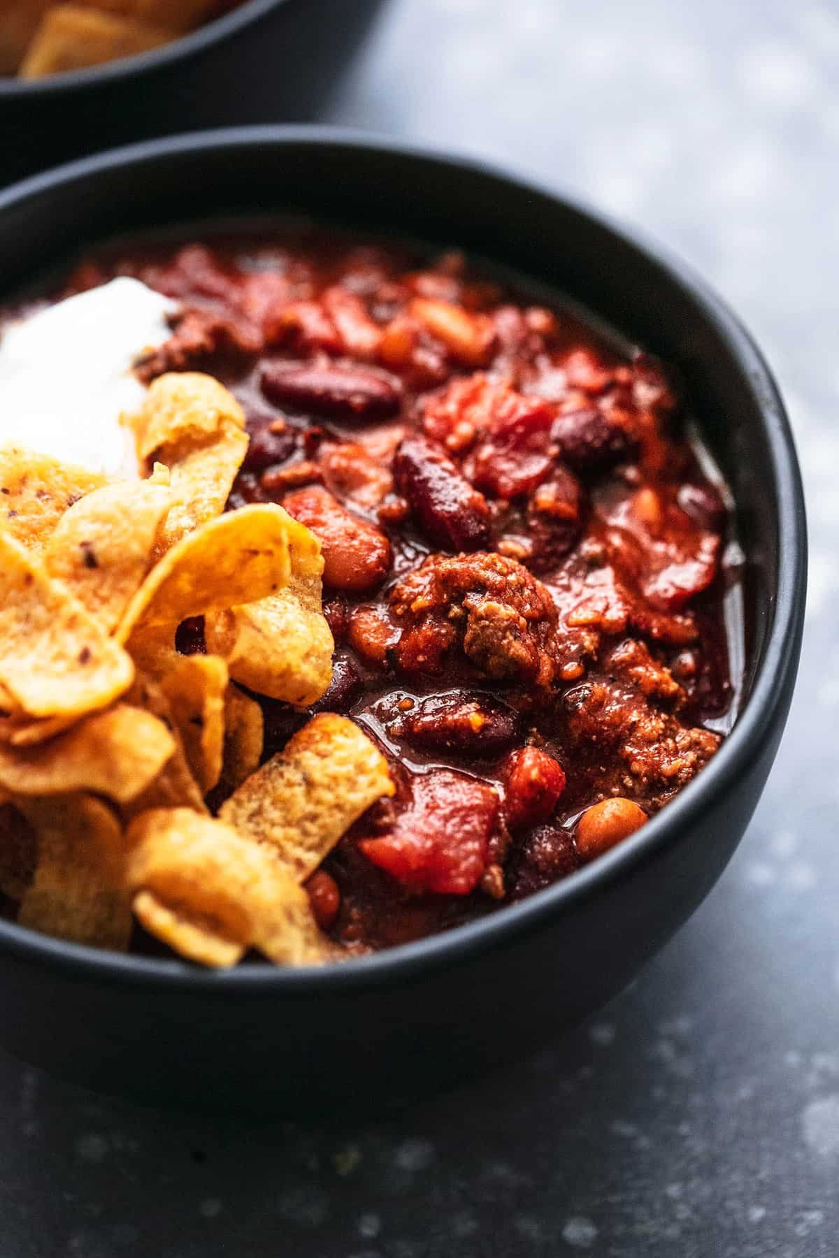 close up of chili with Fritos and sour cream on the side all in a bowl.