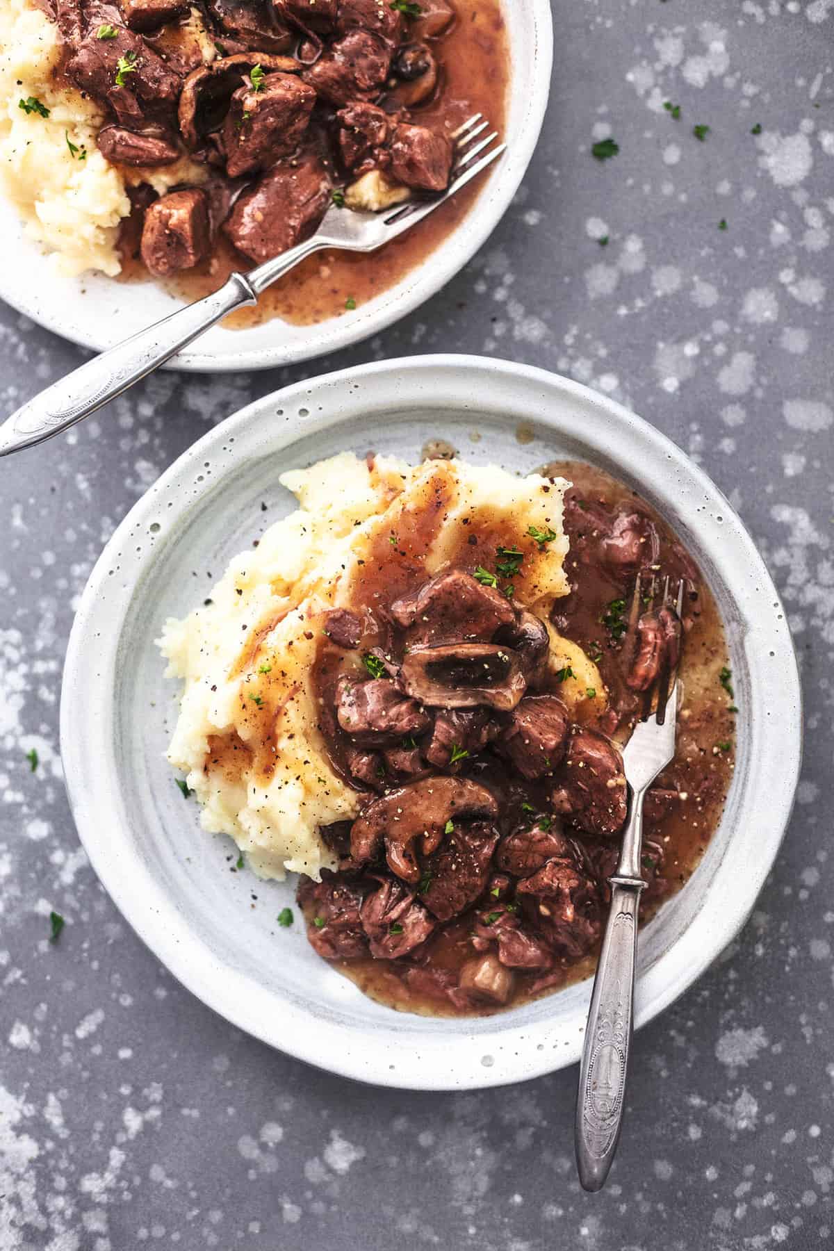 top view of instant pot beef tips with mashed potatoes and a fork on a plate with another plate on the side.