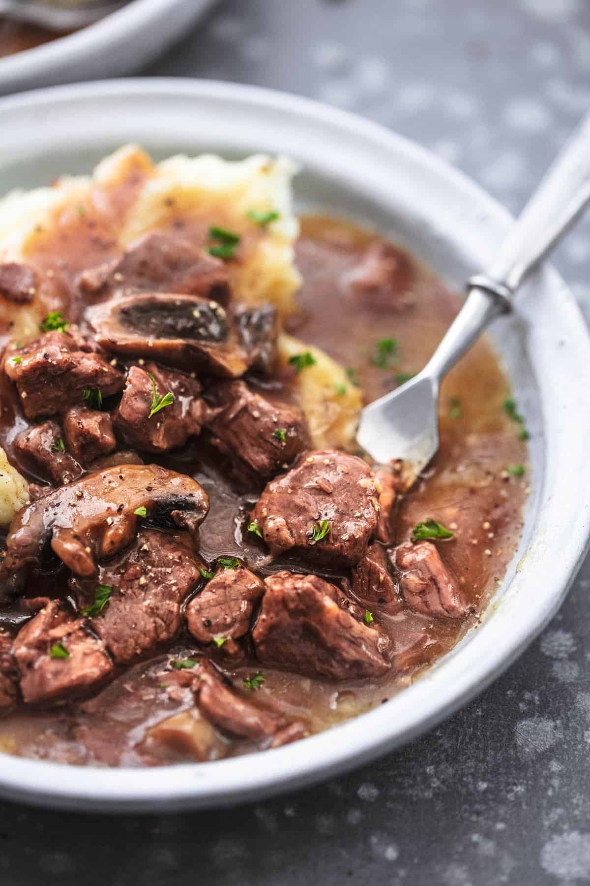close up of instant pot beef tips with a fork and mashed potatoes on a plate.