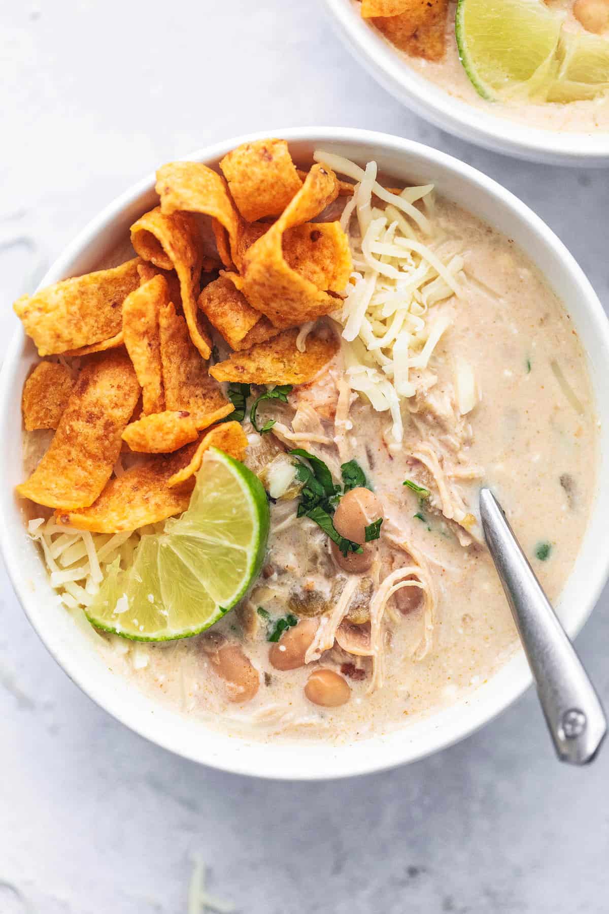 top view of instant pot white chicken chili with Fritos, a lime slice, and a spoon in a bowl.