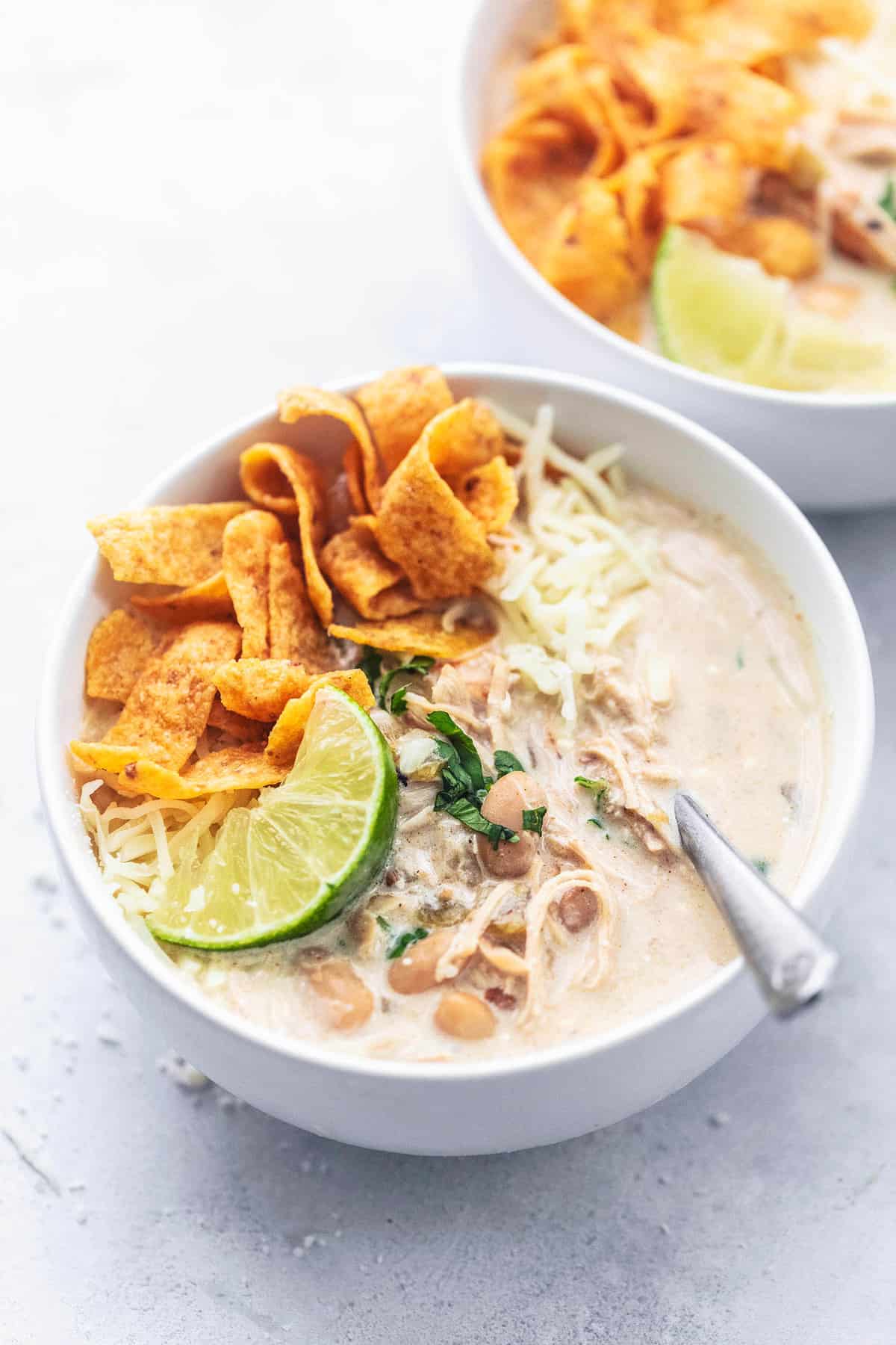 instant pot white chicken chili with Fritos, a lime slices, and a spoon in a bowl with another bowl off to the side.