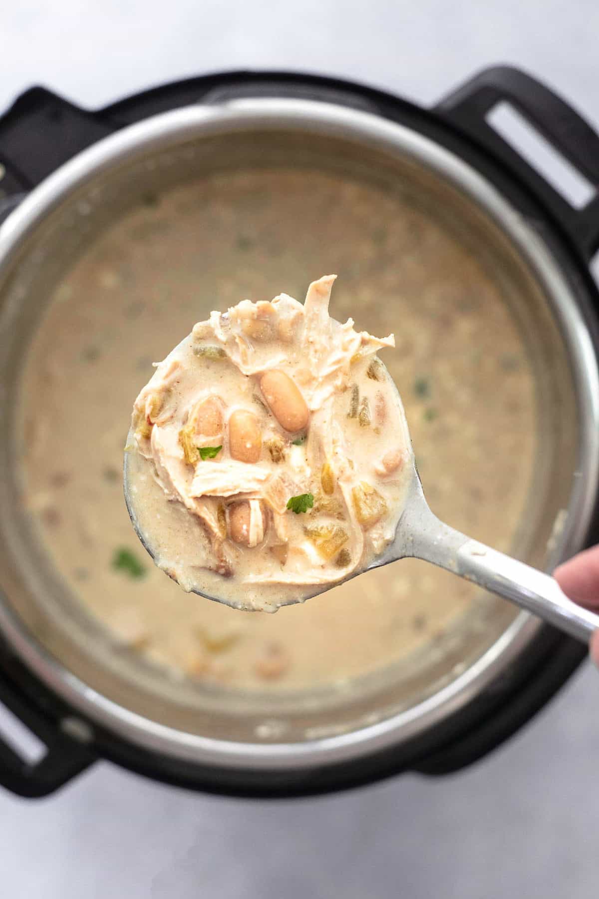 top view of a scoop of instant pot white chicken chili on a serving spoon being held above an instant pot with more chili.