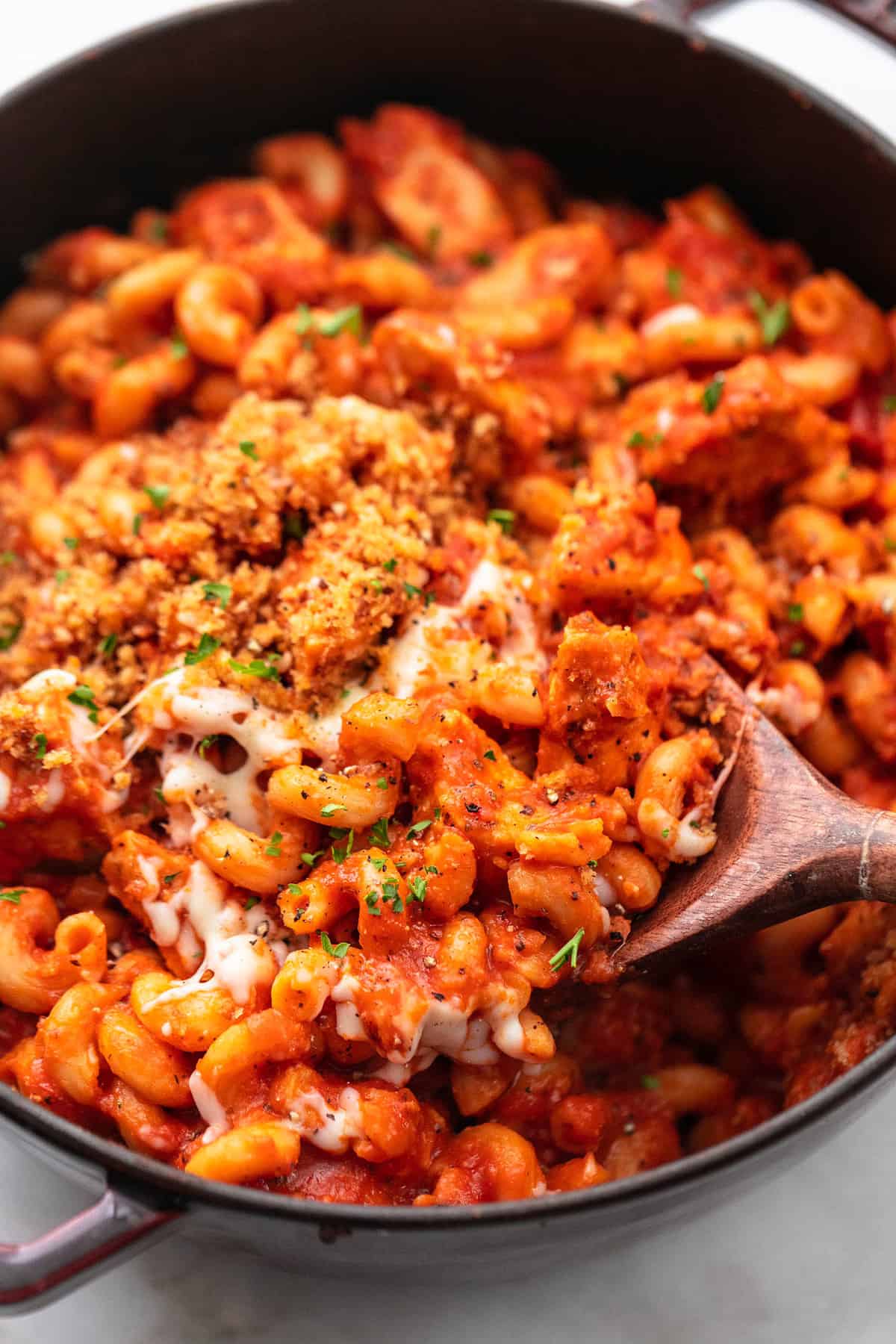 close up of chicken parmesan pasta with a wooden serving spoon in a pan.