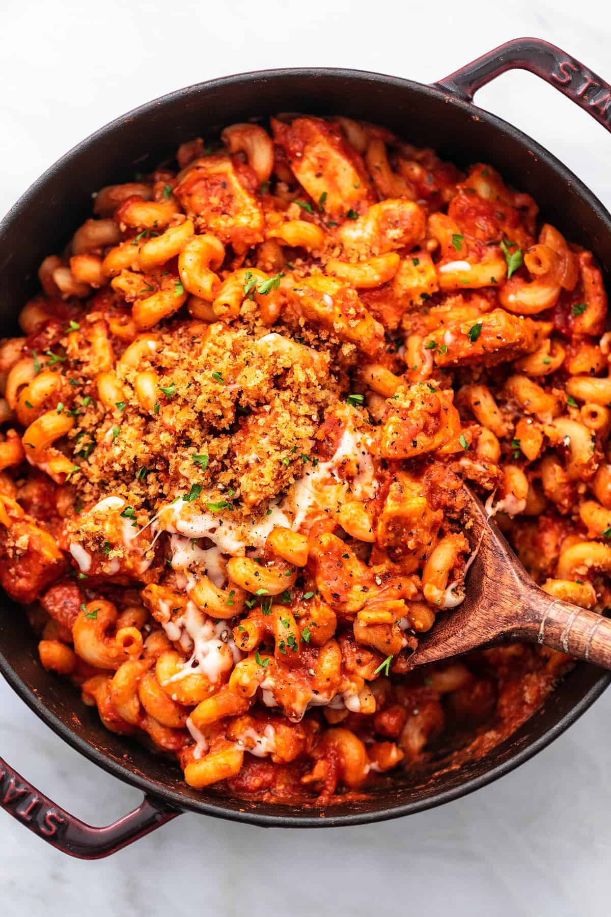 top view of chicken parmesan pasta with a wooden serving spoon in a pan.