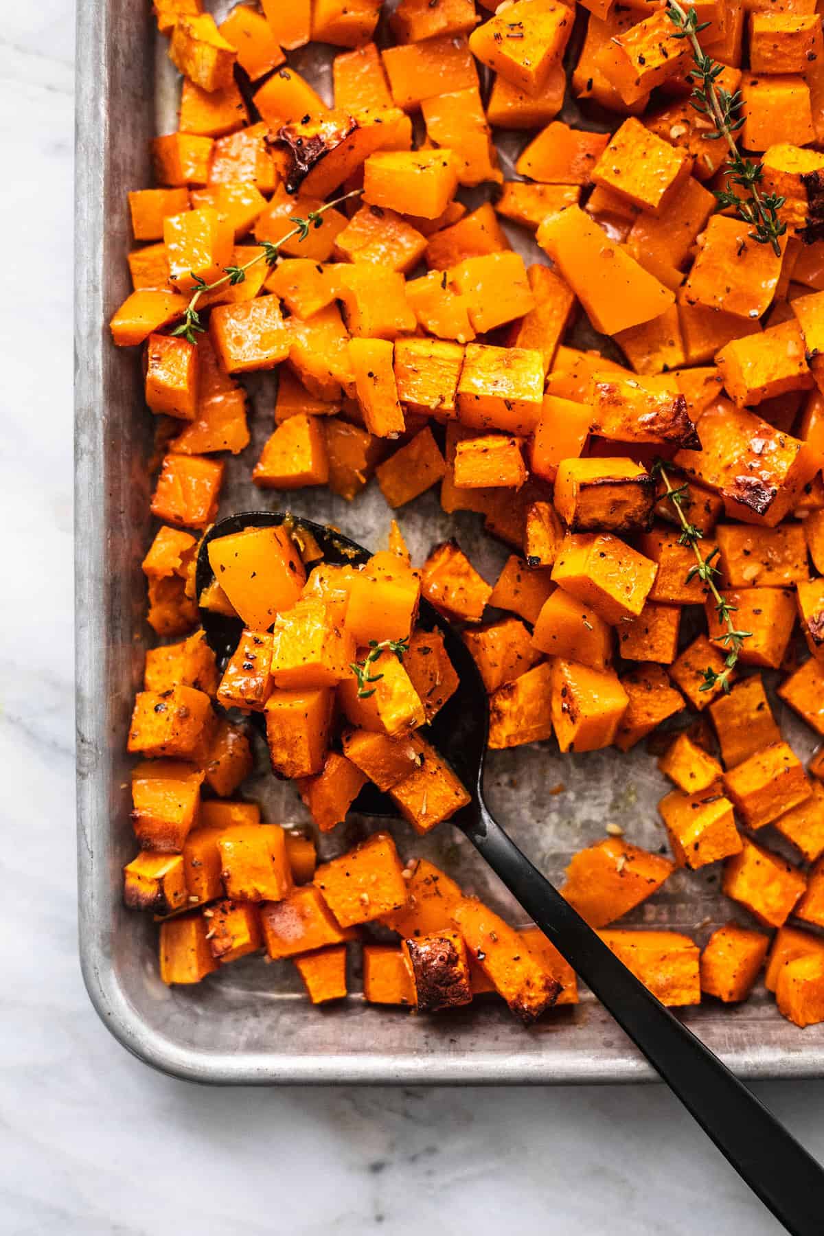 close up top view of roasted butternut squash with a serving spoon on a baking sheet.