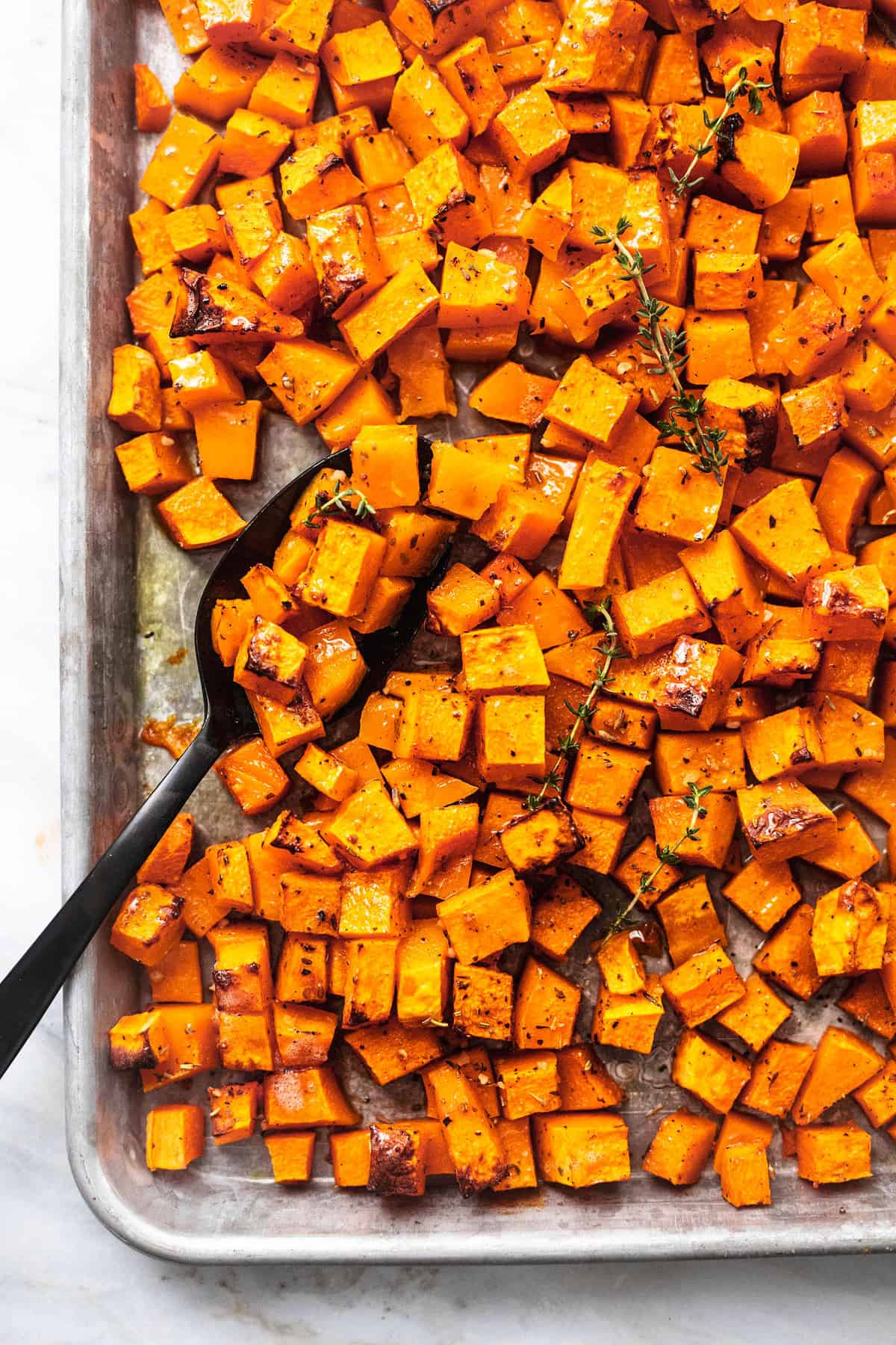 close up top view of roasted butternut squash with a serving spoon on a baking sheet.