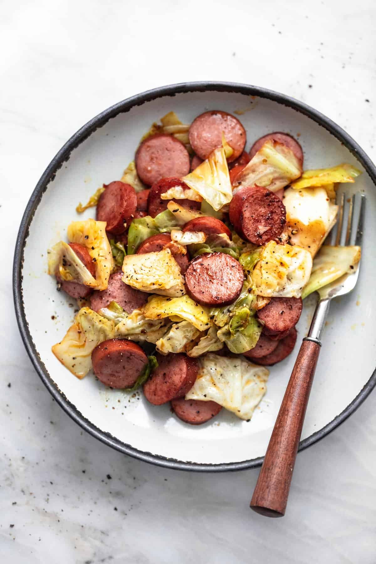 top view of sausage and cabbage skillet with a fork on a plate.