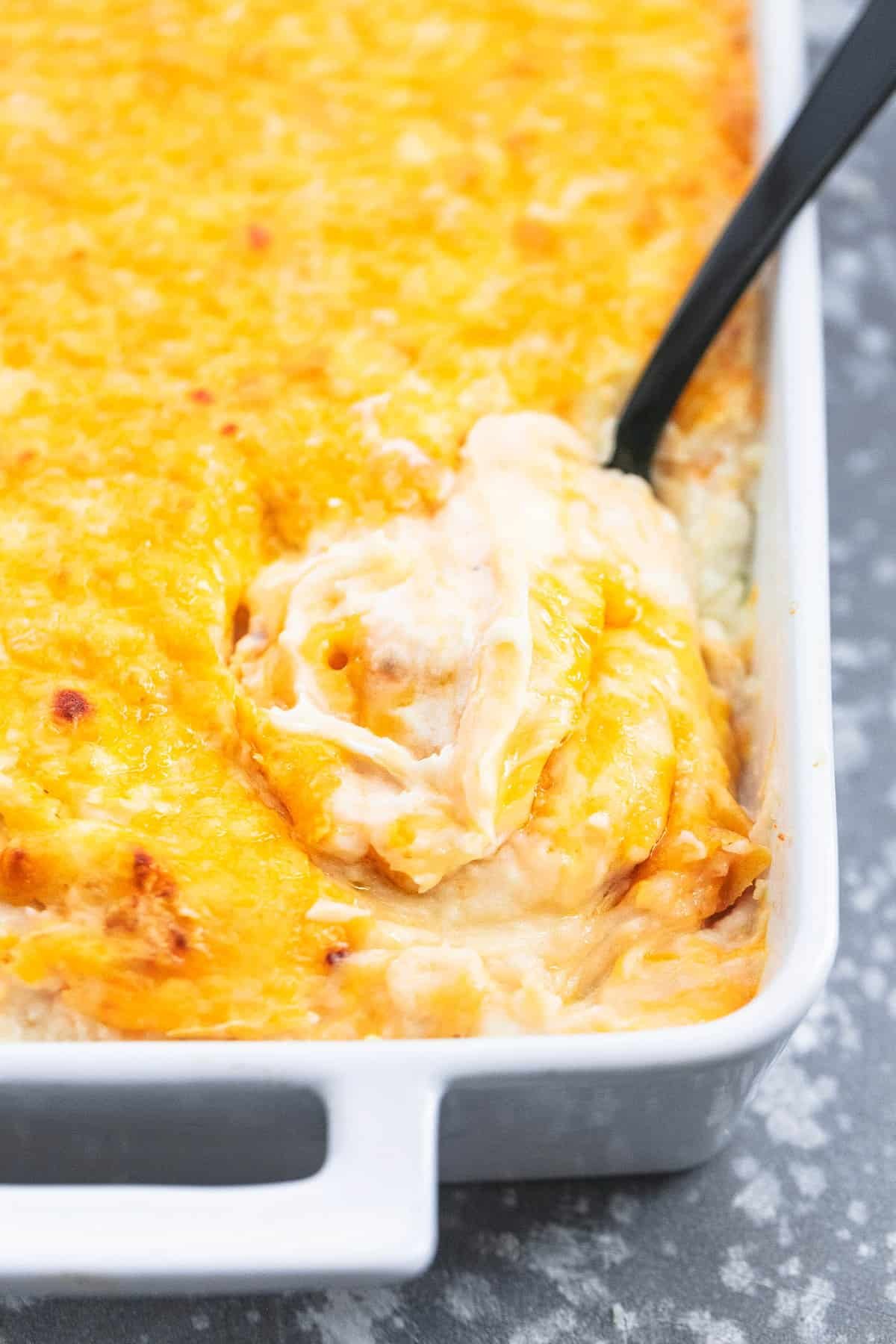 close up of cheesy mashed potatoes casserole with a serving spoon in a baking pan.