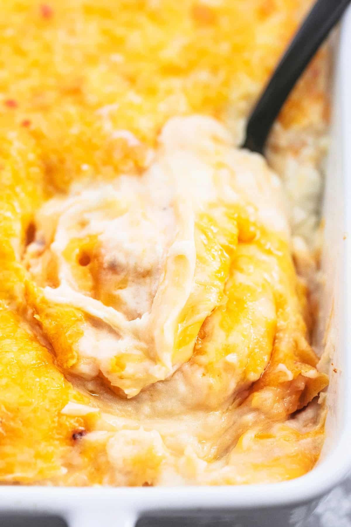 close up of cheesy mashed potatoes casserole with a serving spoon in a baking pan.