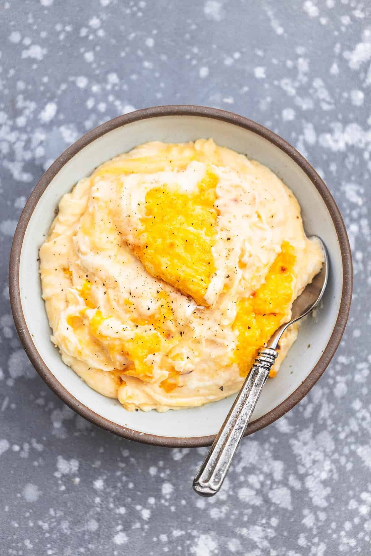 top view of cheesy mashed potatoes casserole with a spoon in a bowl.