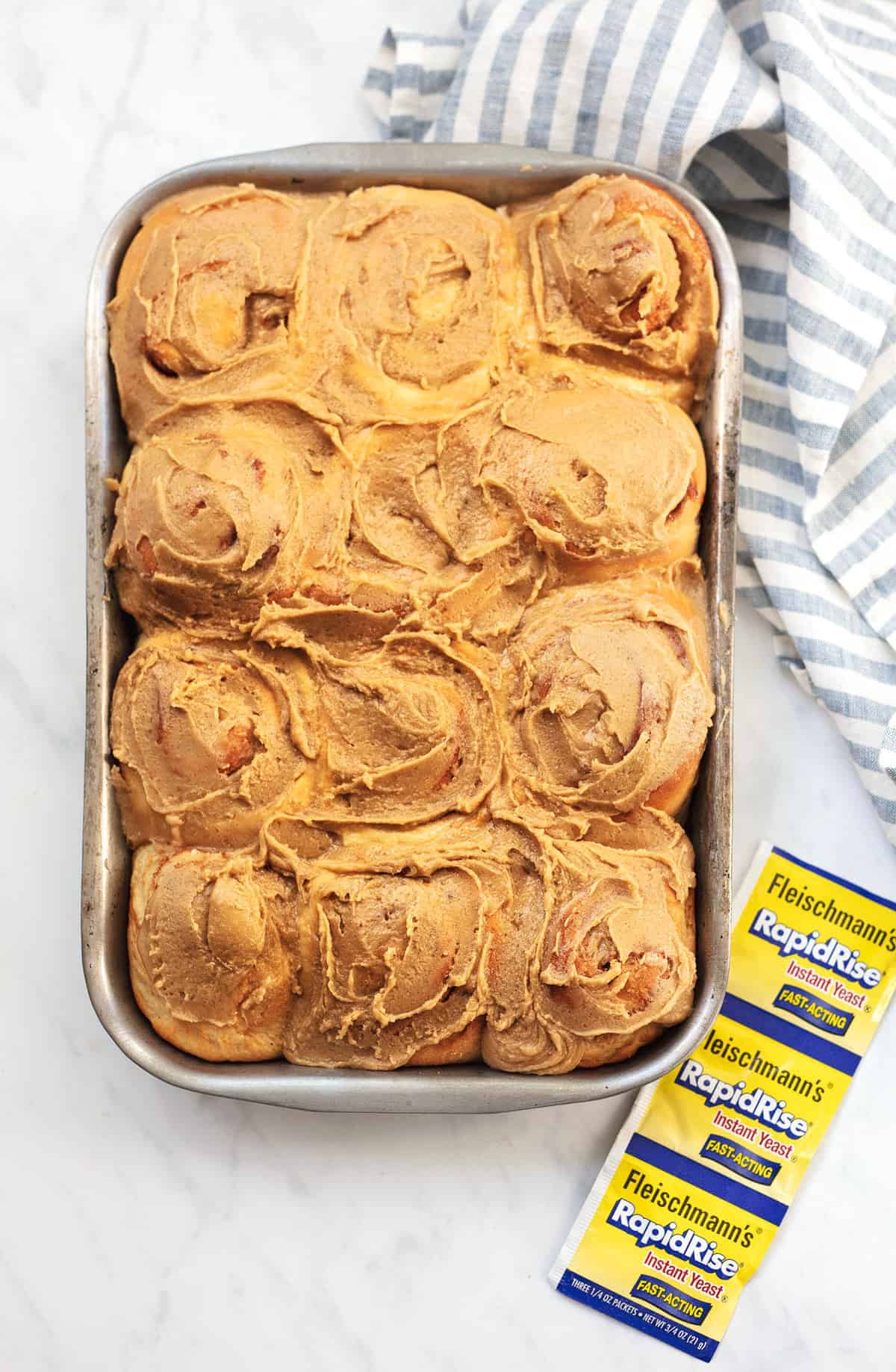 top view of cinnamon rolls with brown sugar frosting in a baking pan with packages of RapidRise yeast on the side.