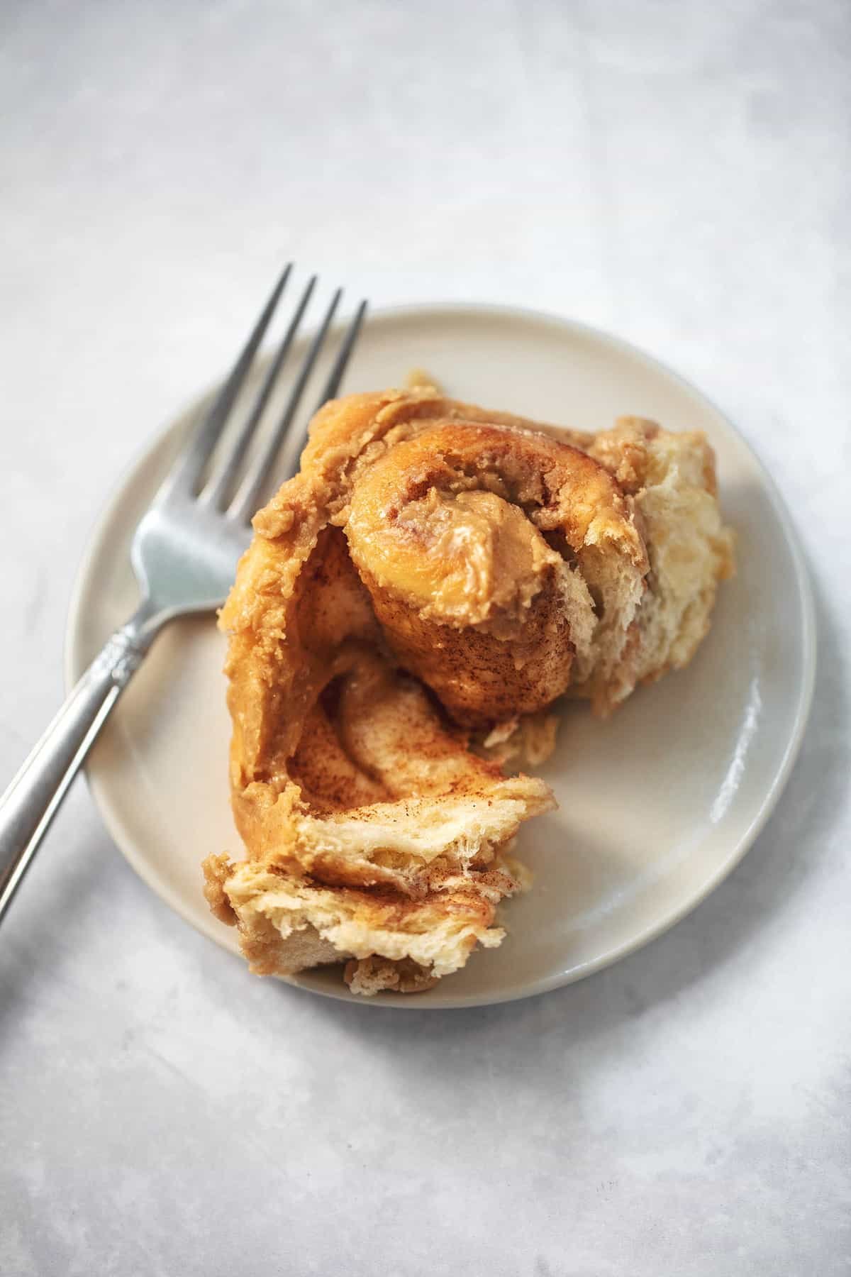 a cinnamon roll with brown sugar frosting with a bite missing and a fork on the side both on a plate.
