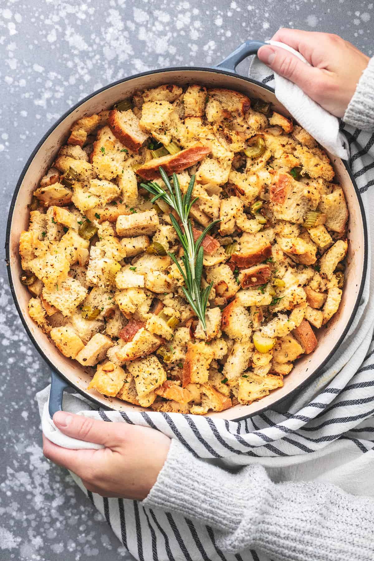 top view of a pair of hands holing the handles of a pan of homemade stuffing.