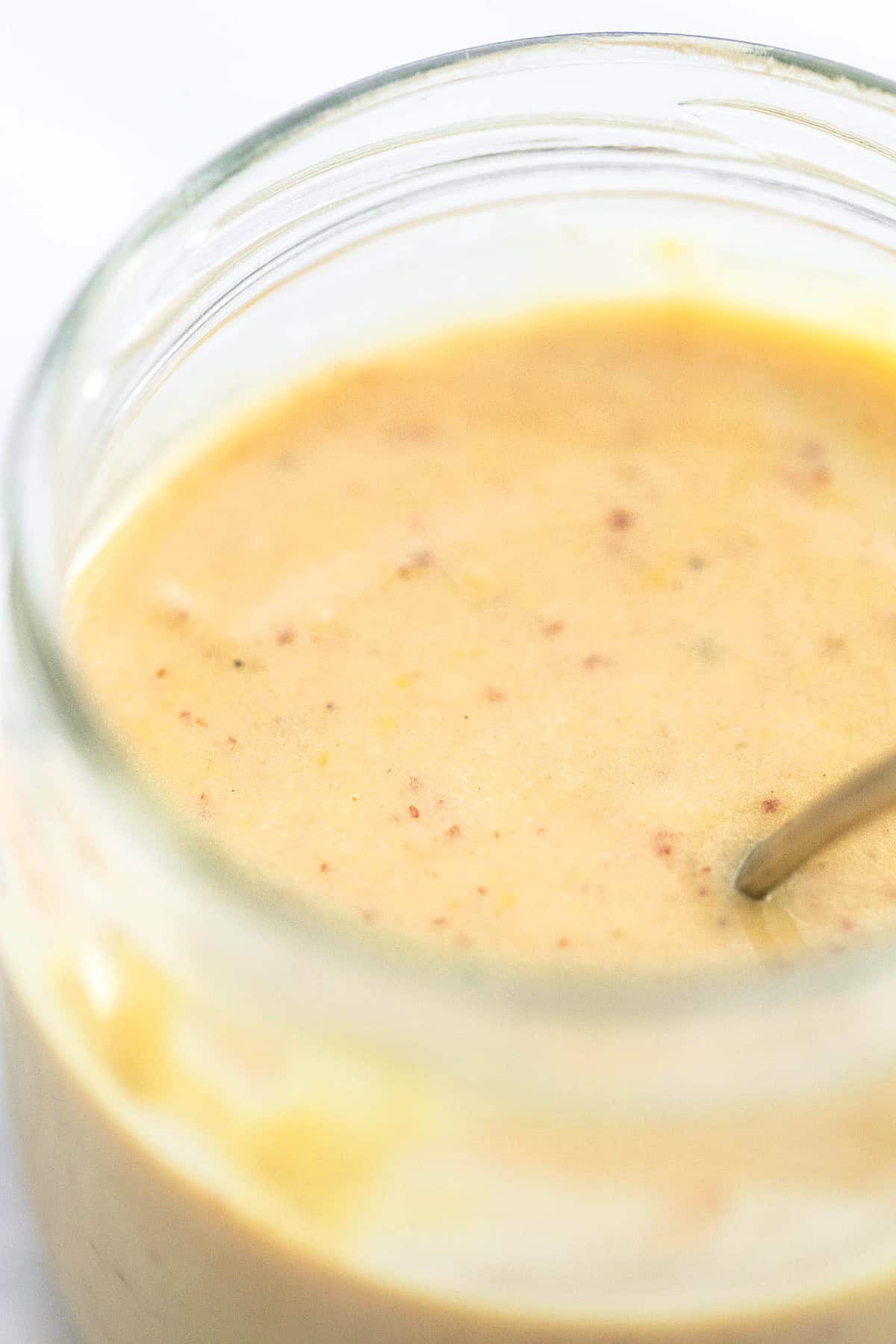 close up of fat free Dijon salad dressing with a spoon in a glass.