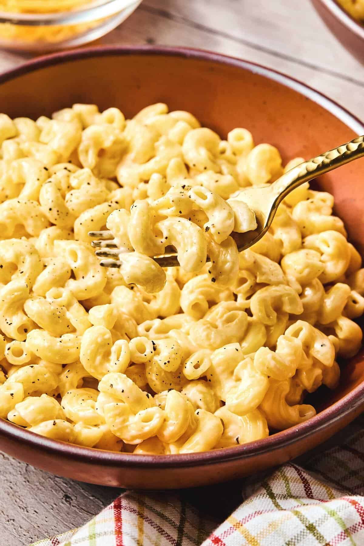 Instant pot mac and cheese in a bowl with a fork being lifted from it with noodles on it.