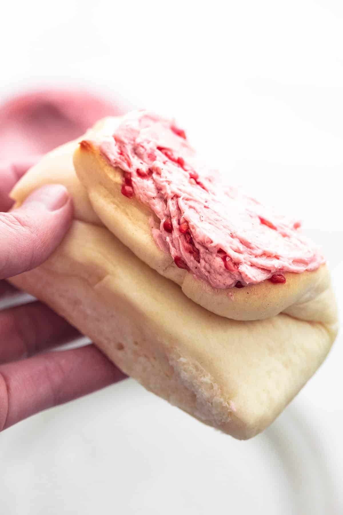 a hand holding a homemade Parker House roll with raspberry almond butter on top.