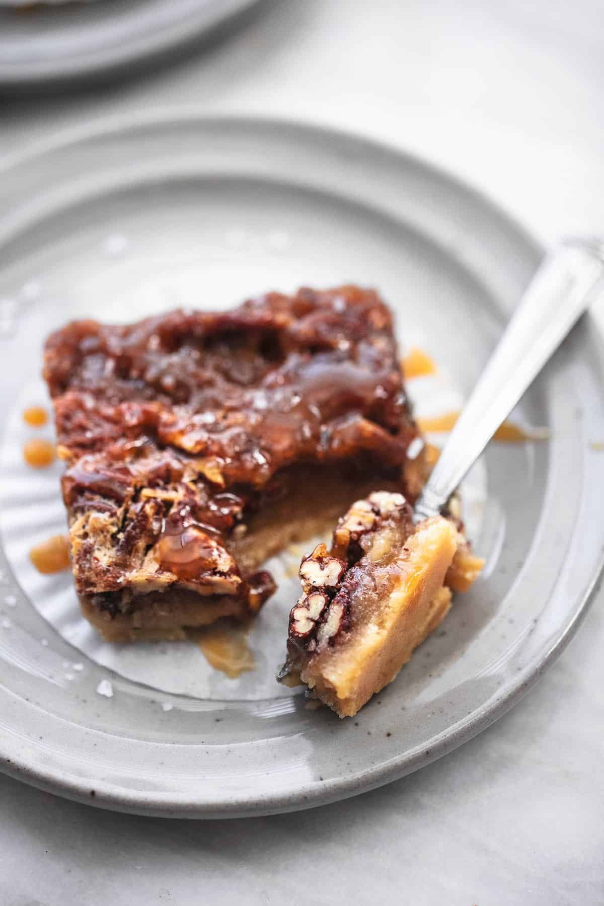 a bite of a salted caramel pecan pie bar on a fork with the rest of the bar both on a plate.