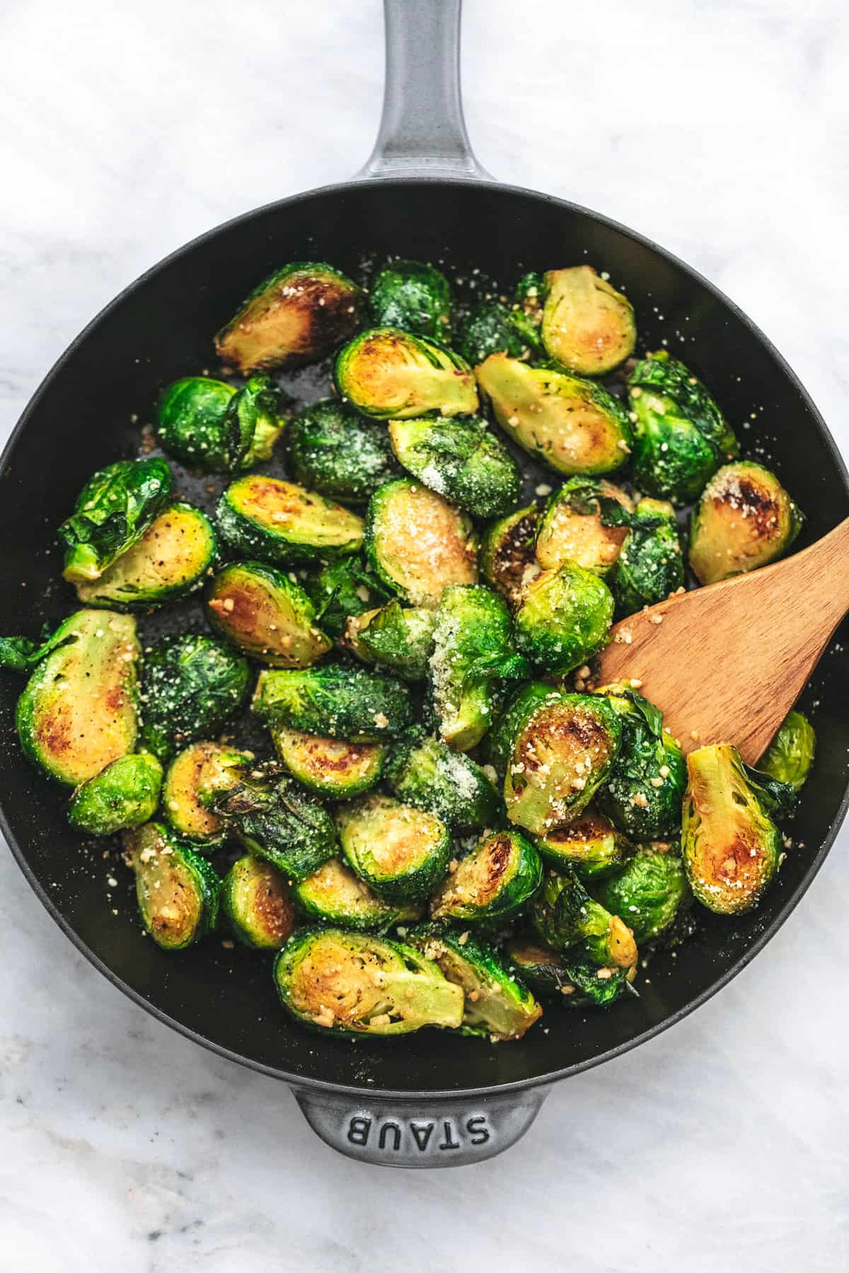 top view of sautéed brussels sprouts with a wooden serving spoon in a pan.
