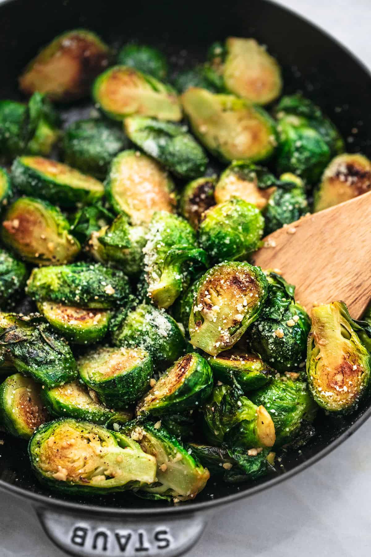close up of sautéed brussels sprouts with a wooden serving spoon in a pan.