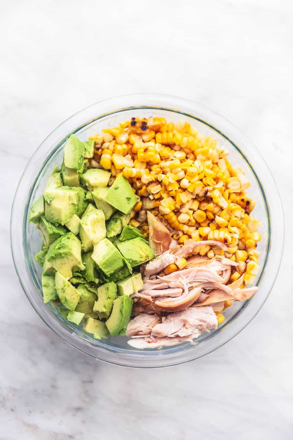top view of chicken avocado corn salad ingredients in a glass bowl.