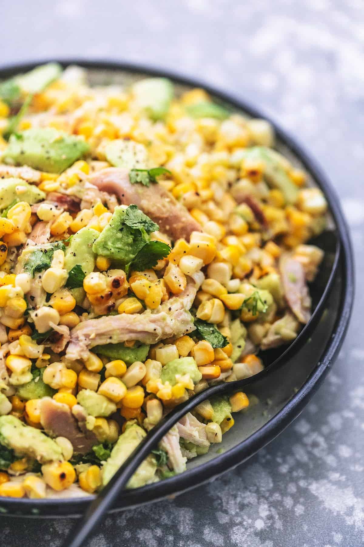 close up of chicken avocado corn salad with a serving spoon on a plate.