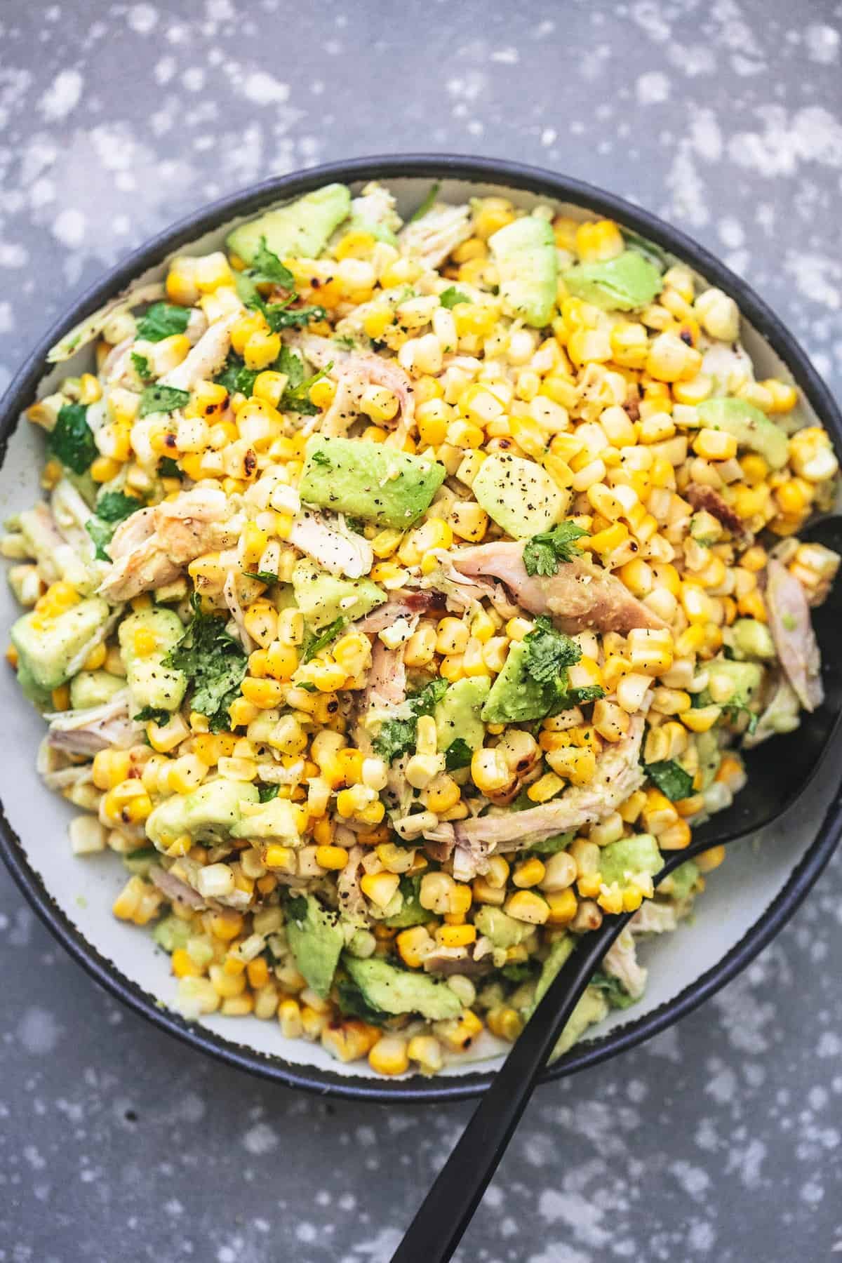 top view of chicken avocado corn salad with a serving spoon on a plate.
