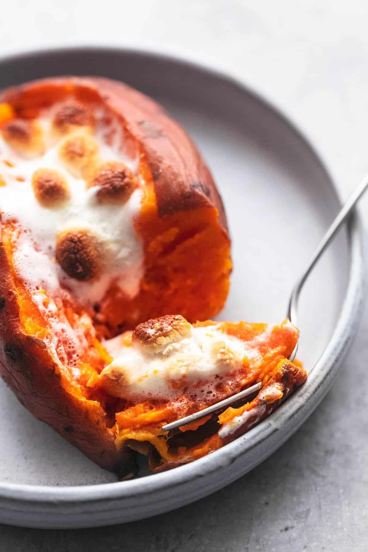 a instant pot baked sweet potato with a bite of it on a fork both on a plate.