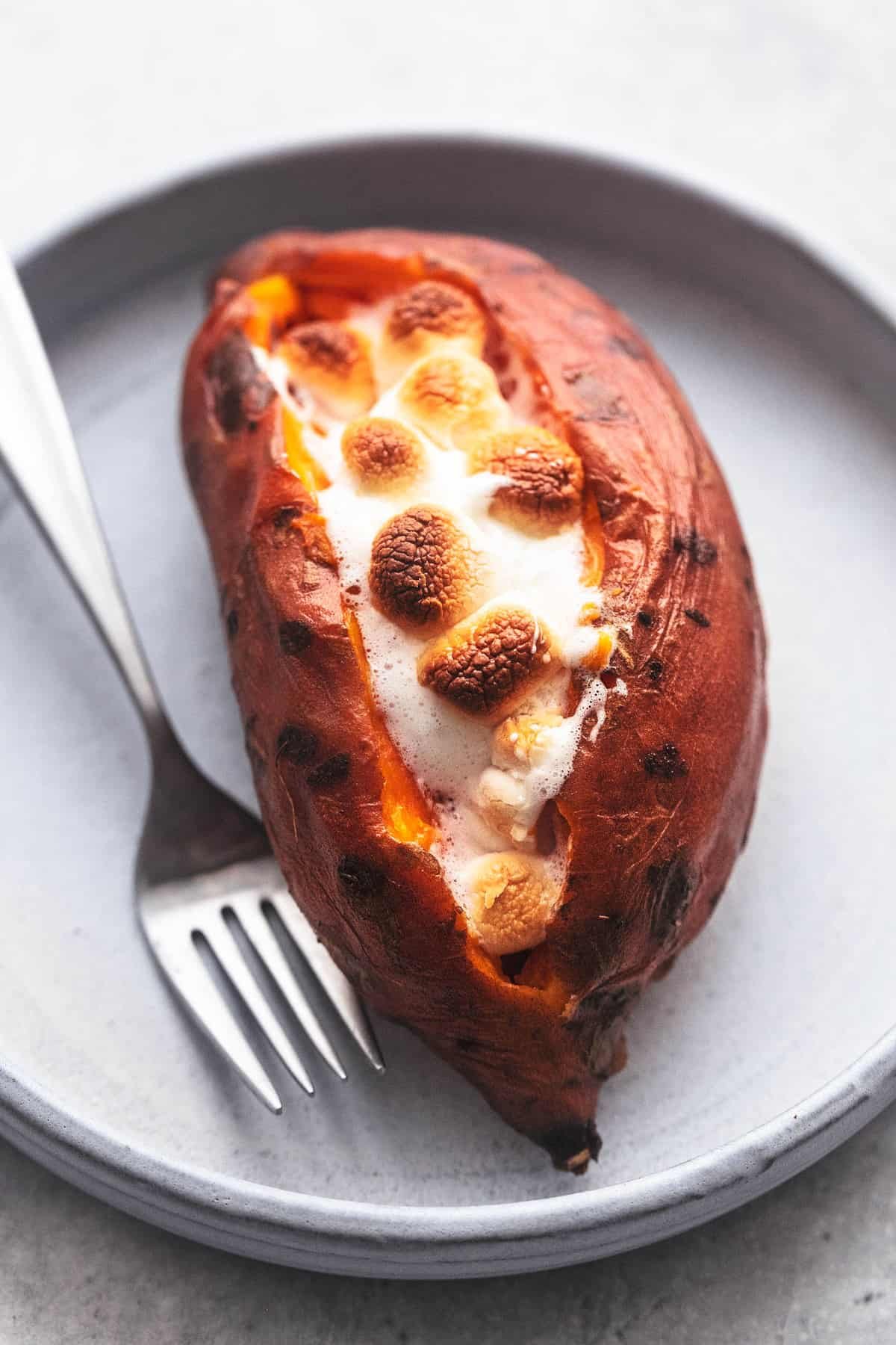 a instant pot baked sweet potato topped with marshmallows with a fork on a plate.