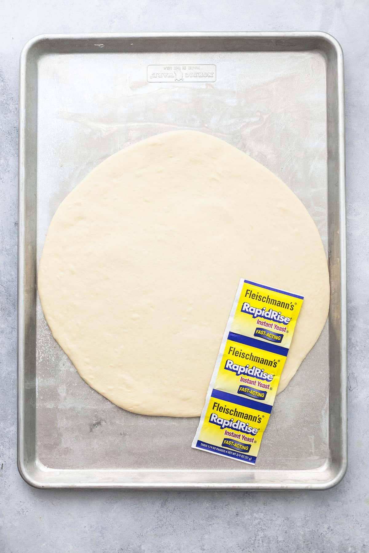 top view of pizza dough on a baking sheet in RapidRise yeast packets sitting on top of the dough.