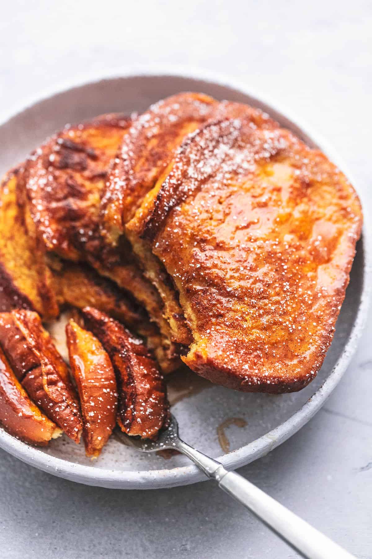 stacked pumpkin French toast with a bite missing with the bite on a fork both on a plate.