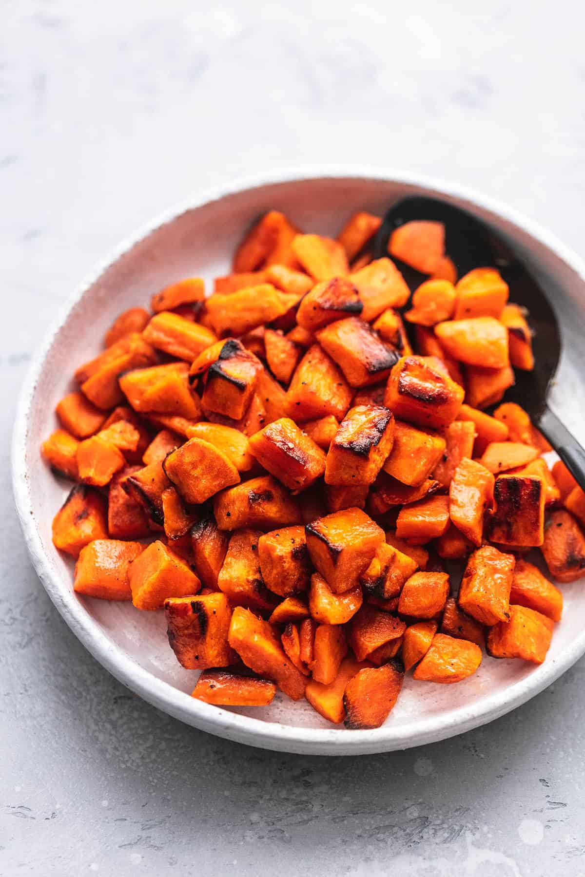 roasted sweet potatoes  with a serving spoon on a plate.