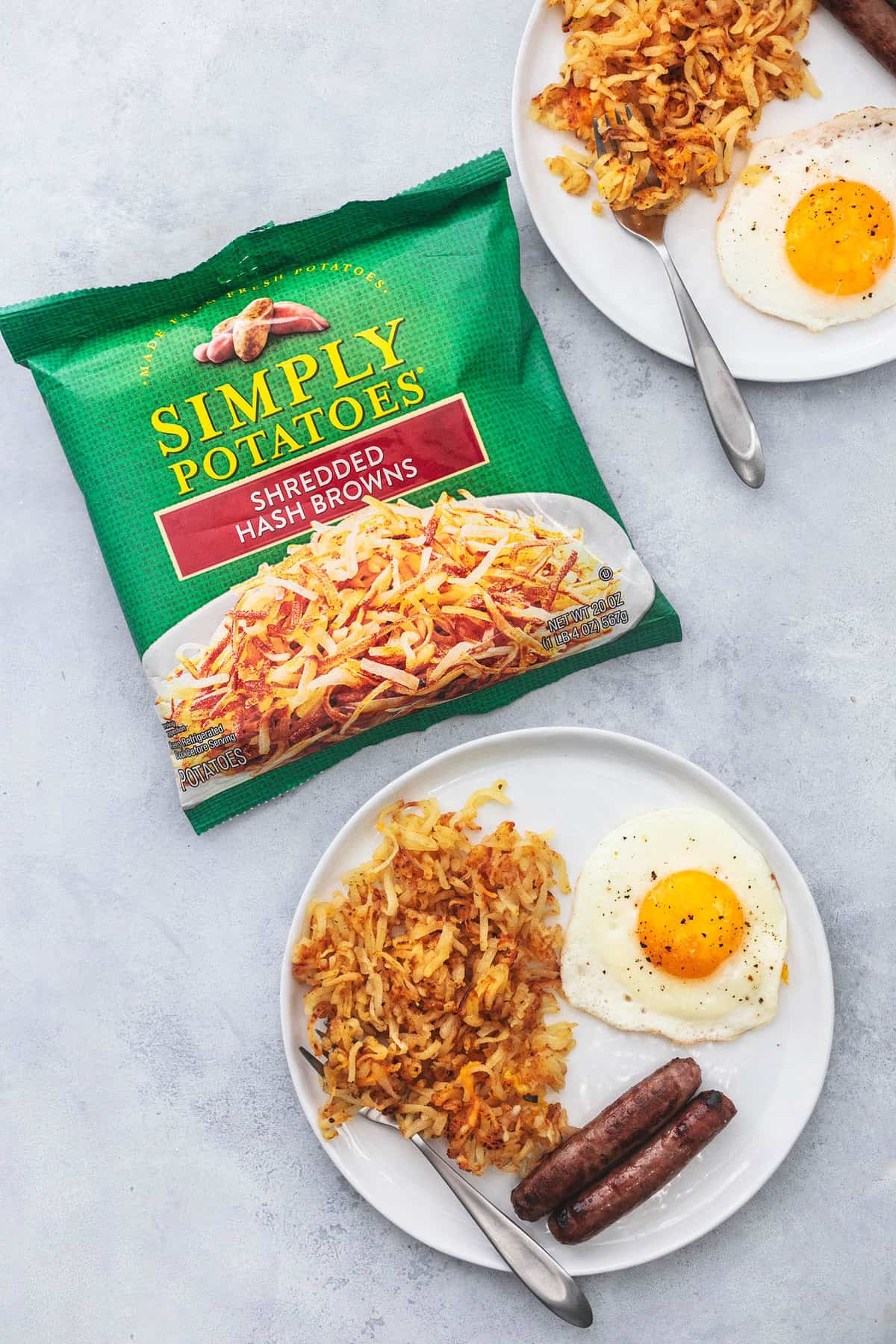 top view of sheet pan breakfast with a fork on a plate with a package of Simply Potatoes and another plate of breakfast and a fork on a plate on the side.